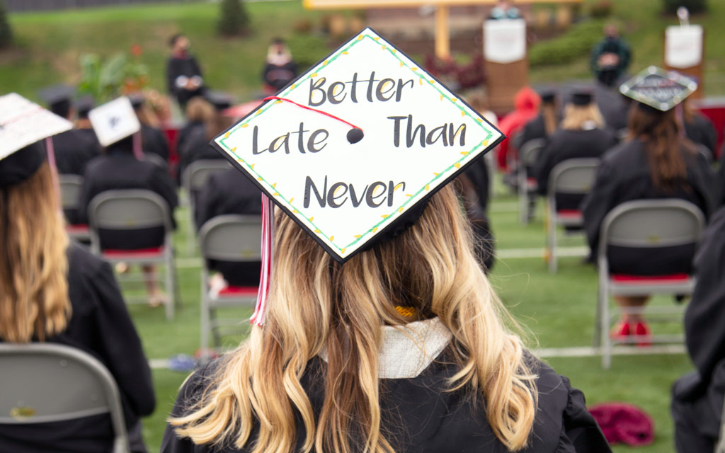 Student at Commencement with a mortarboard reading, "Better Late Than Never."