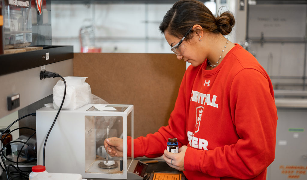 Female student in red sweatshirt working in a chemistry lab