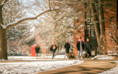 Campus with snow and five students walking outside.