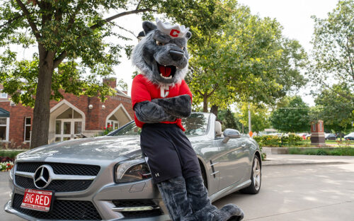 Big Red Mascot leaning against a gray car