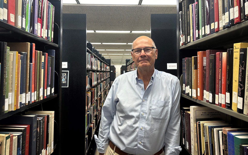 Harry Smith '73 leaning along books in Geisler Library. 2024